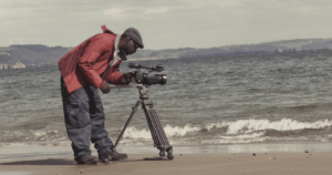 warsztaty filmowe ujęcie nad morzem mężczyzna pochyla się nad profesjonalną kamerą na statywie